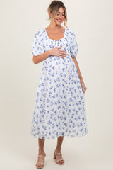 woman wearing a white floral maternity dress with puff sleeves and holding her baby bump