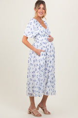 woman wearing a white floral maternity dress with puff sleeves, cinched waist, and pockets, showing her baby bump