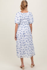 woman wearing a white floral print maternity dress with puff sleeves and a cinched waist, showing her baby bump