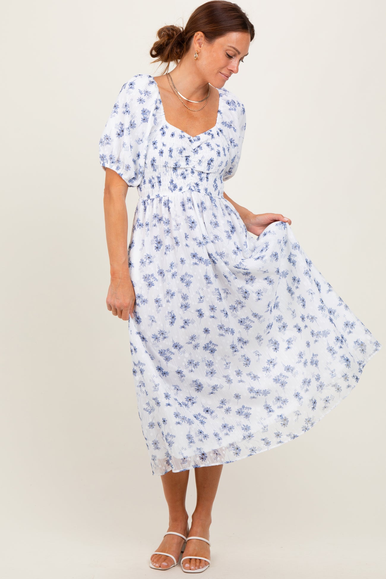 woman wearing a white floral maxi dress with puff sleeves, standing gracefully and holding the skirt gently