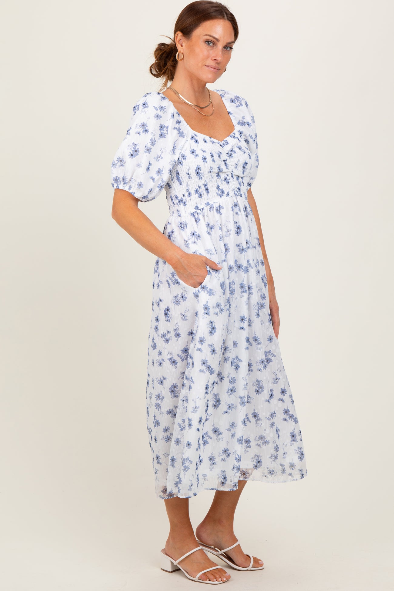 woman wearing a white floral midi dress with puff sleeves and pockets, standing against a neutral background