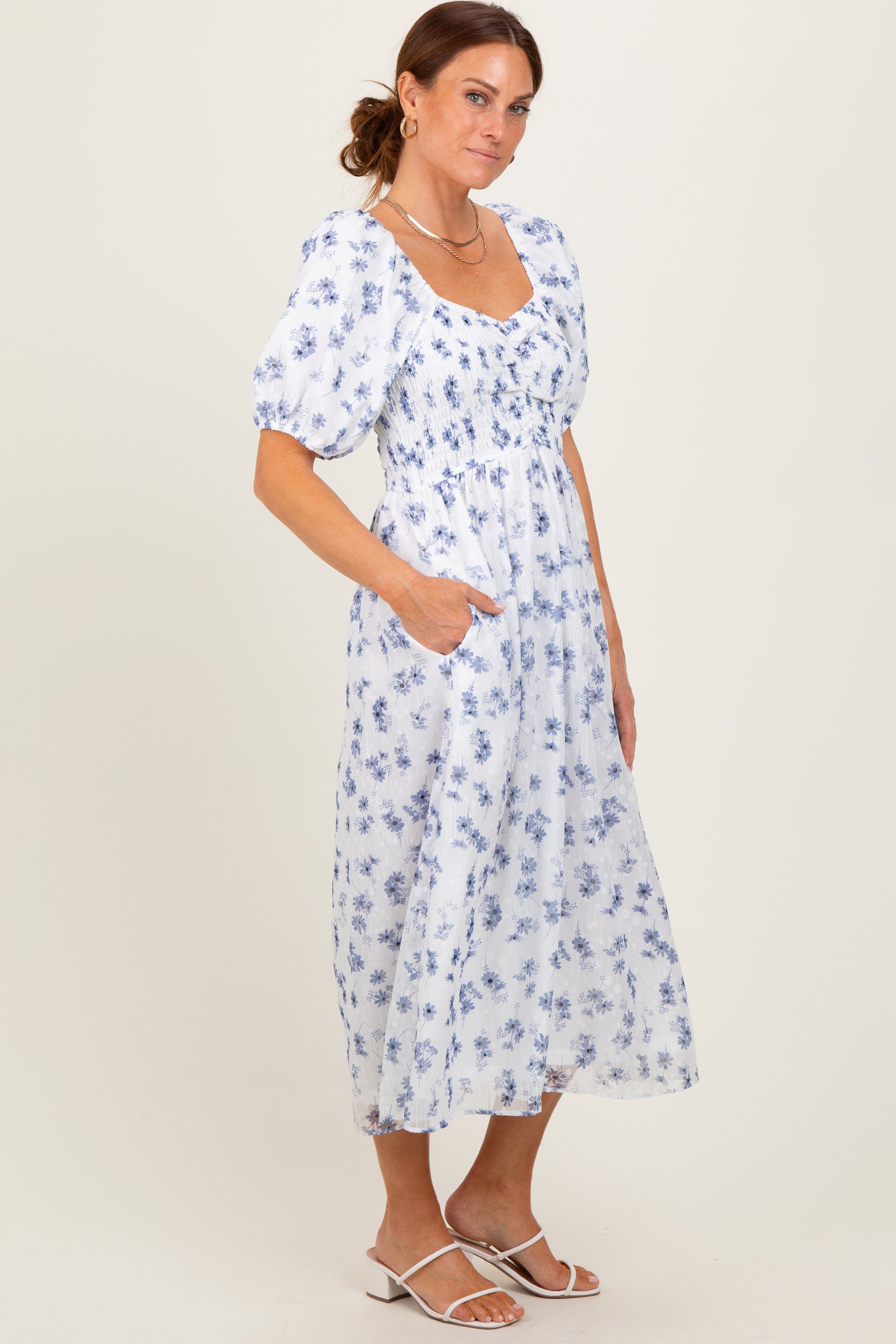 woman wearing a white floral midi dress with puff sleeves and pockets, standing against a neutral background