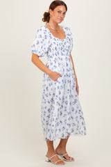 woman wearing a white floral midi dress with puff sleeves and pockets, standing against a neutral background