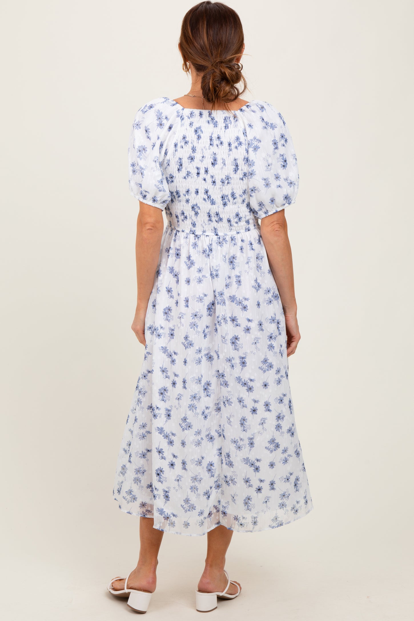 woman wearing a back view of a white maxi dress with blue floral patterns and puff sleeves