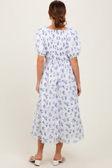woman wearing a back view of a white maxi dress with blue floral patterns and puff sleeves