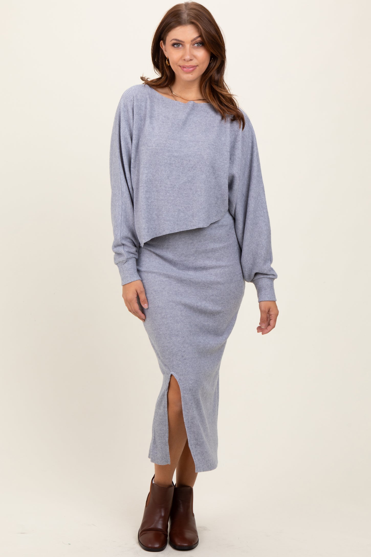 woman wearing a light gray two-piece ribbed sweater dress with a cropped top and a midi skirt featuring a side slit