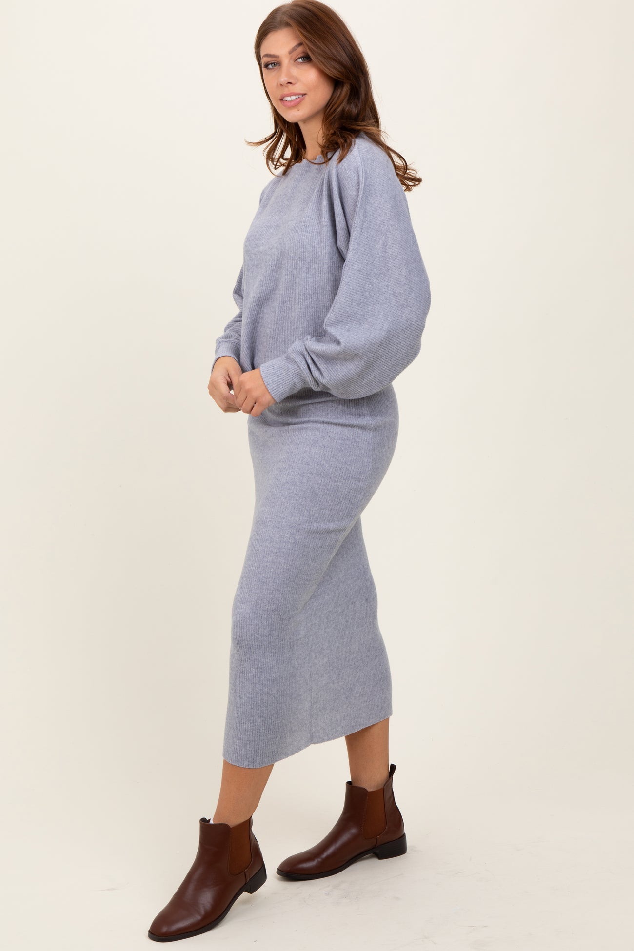 woman wearing a light gray sweater dress with balloon sleeves and brown ankle boots