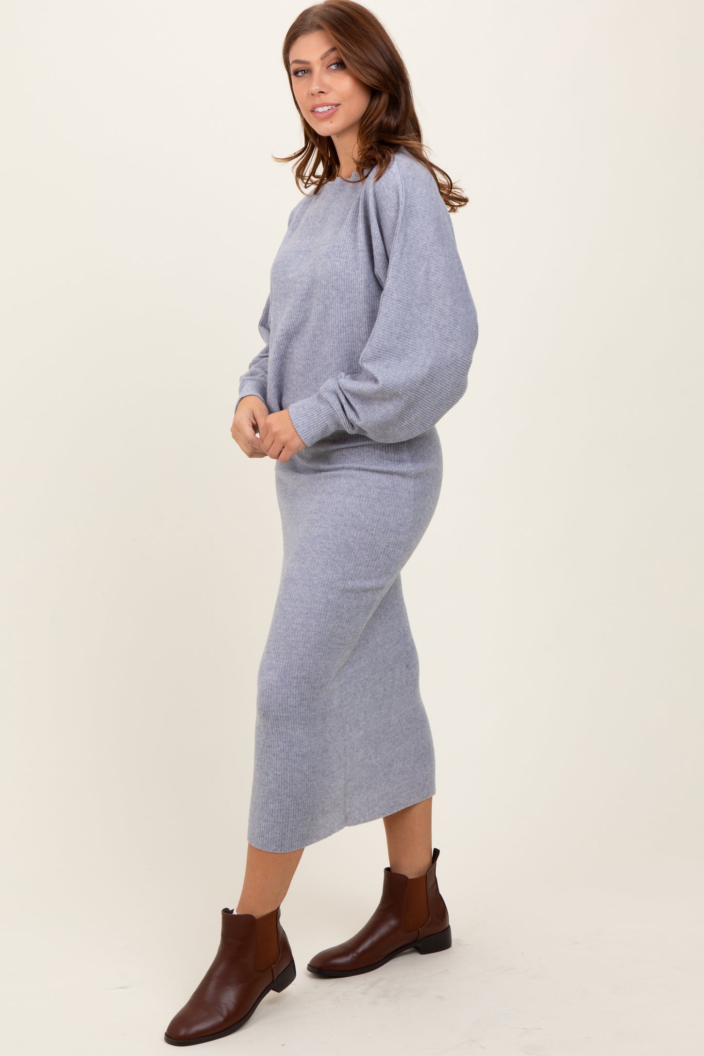 woman wearing a light gray sweater dress with balloon sleeves and brown ankle boots