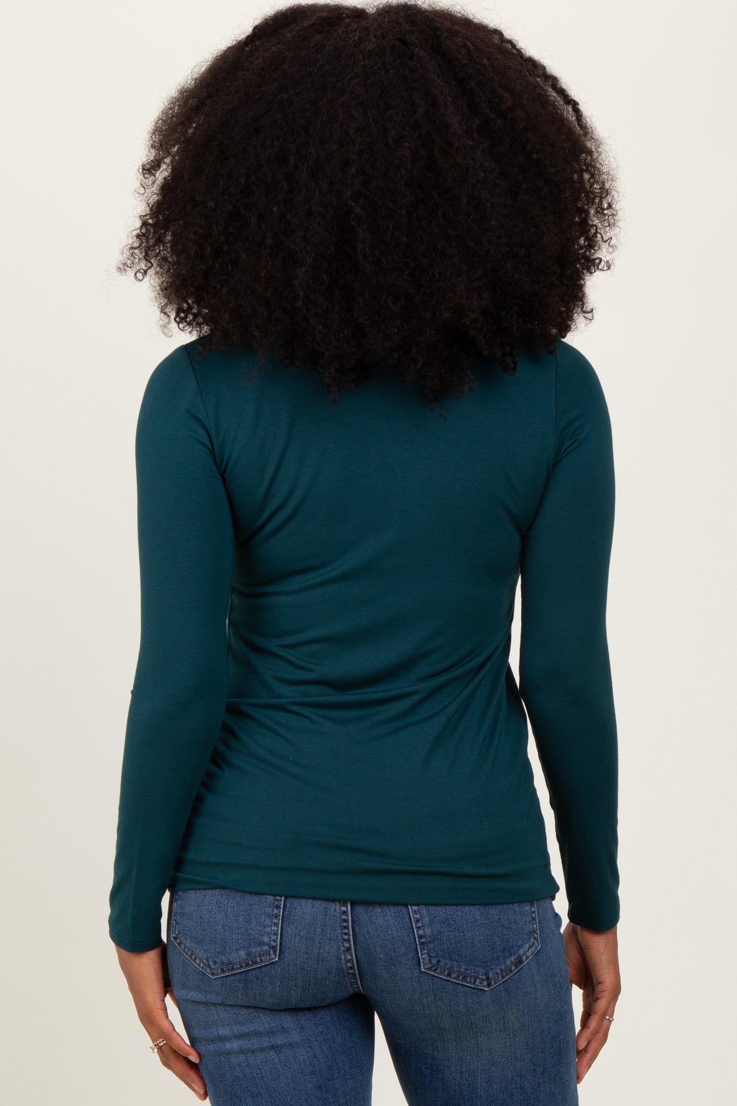 woman wearing a teal long sleeve top with a fitted silhouette, viewed from the back, paired with blue jeans