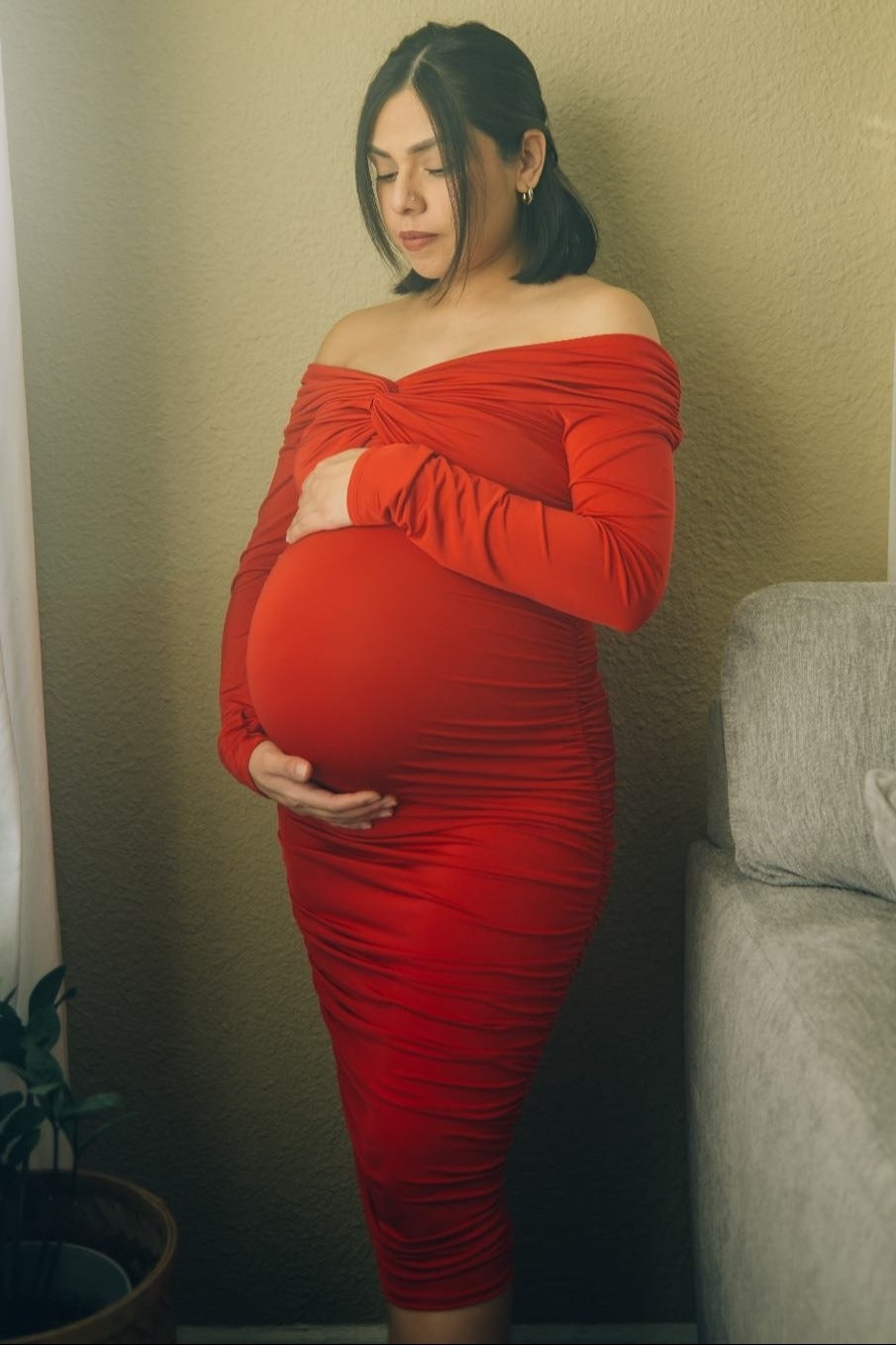 woman wearing a red off-the-shoulder maternity dress and cradling her baby bump