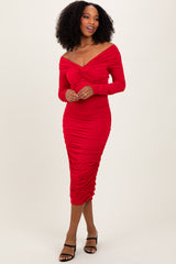 woman wearing a red bodycon dress with long sleeves and twisted front detail, standing with a smile