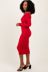 woman wearing a form-fitting red off-the-shoulder midi dress with ruching details and side slit, standing in profile