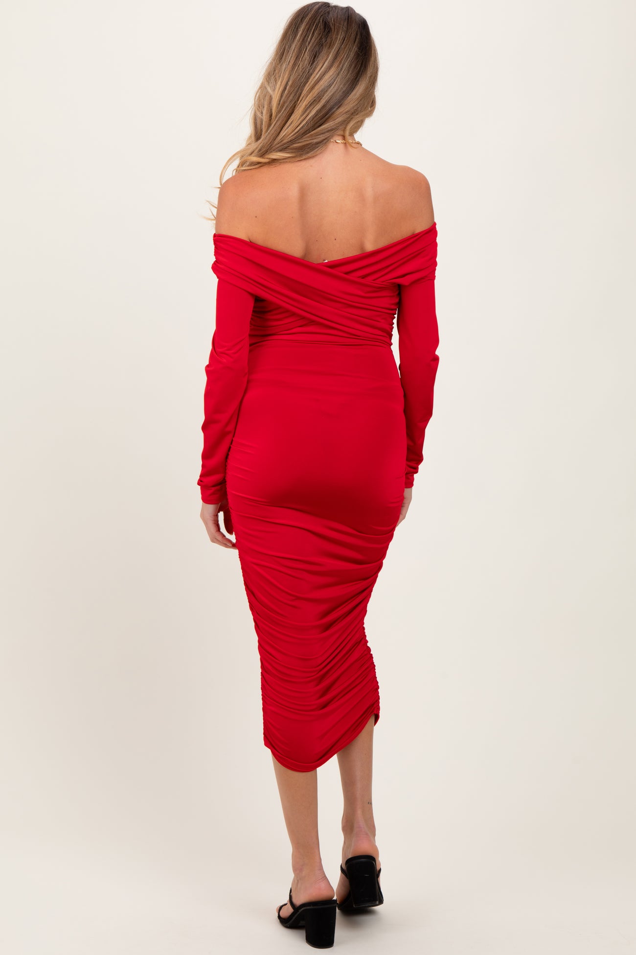 woman wearing a red off-shoulder maternity dress with ruching details, showing her back and hugging her baby bump