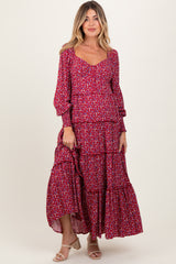 woman wearing a red floral maternity maxi dress with tiered ruffles and bell sleeves, smiling at the camera