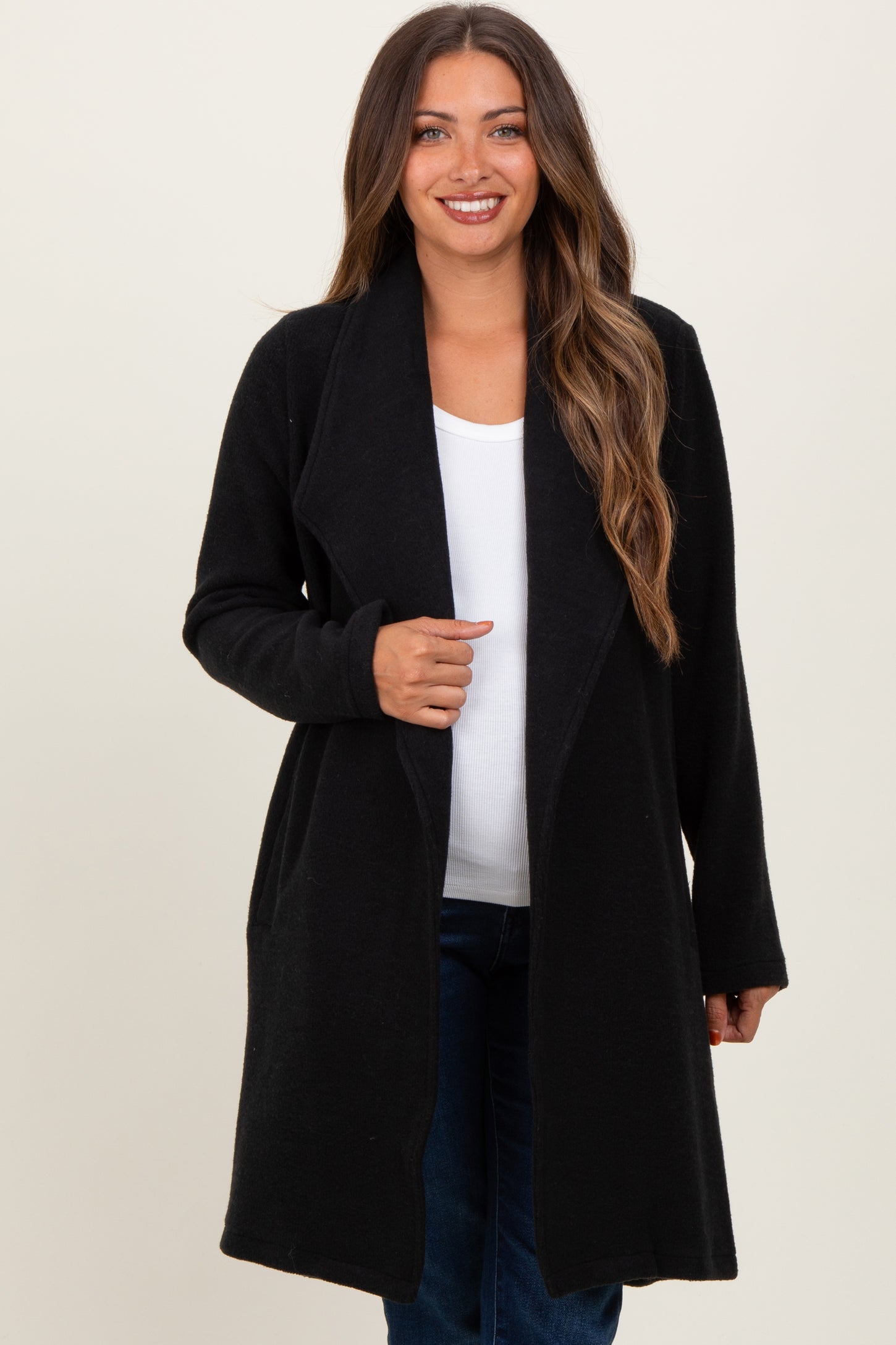 woman wearing a black maternity duster coat over a white top and jeans, smiling at the camera