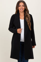 woman wearing a black maternity duster coat over a white top and jeans, smiling at the camera