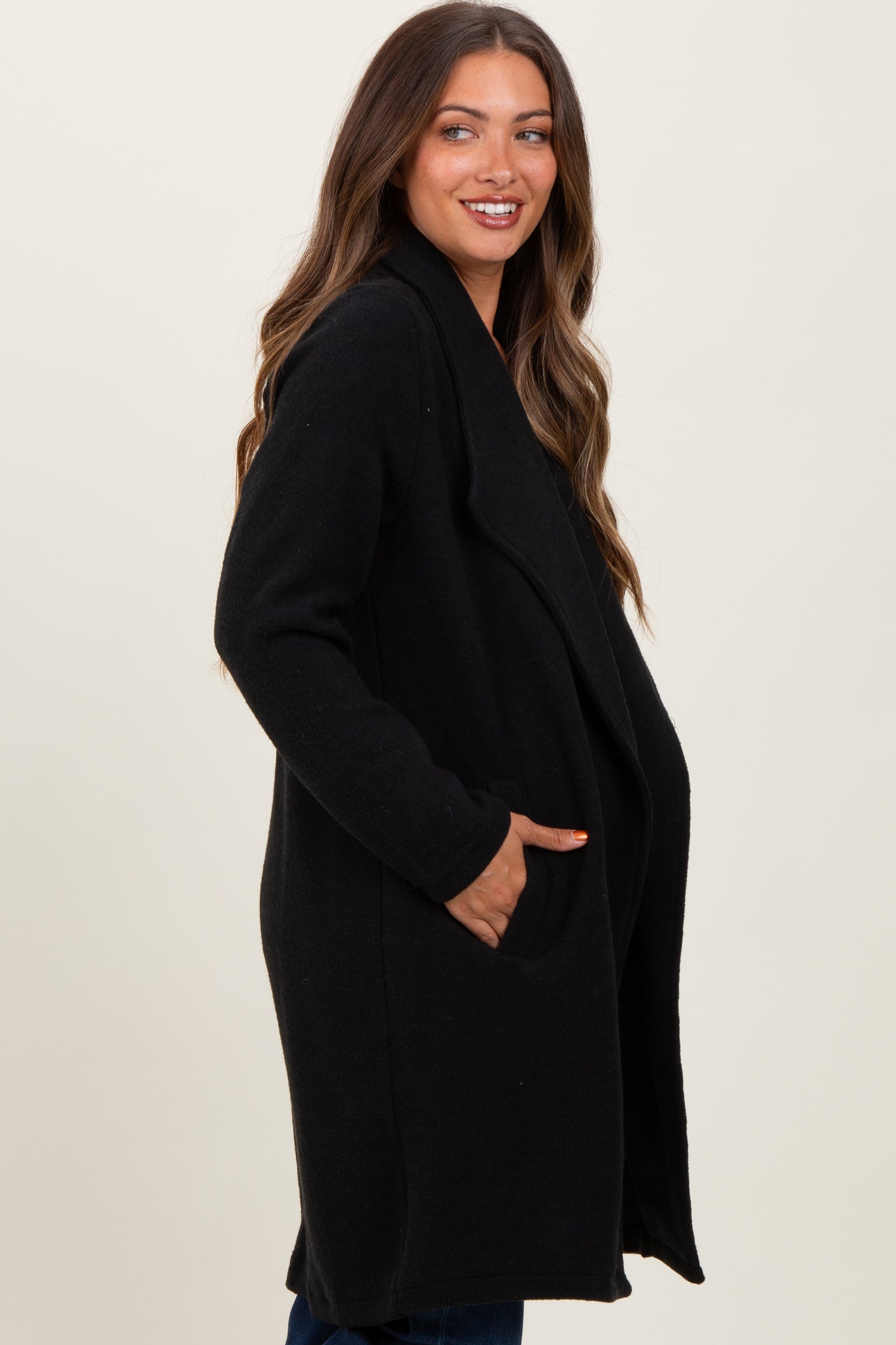 woman wearing a black maternity coat with side pockets and an open front, smiling and standing sideways