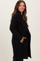 woman wearing a black maternity coat with side pockets and an open front, smiling and standing sideways