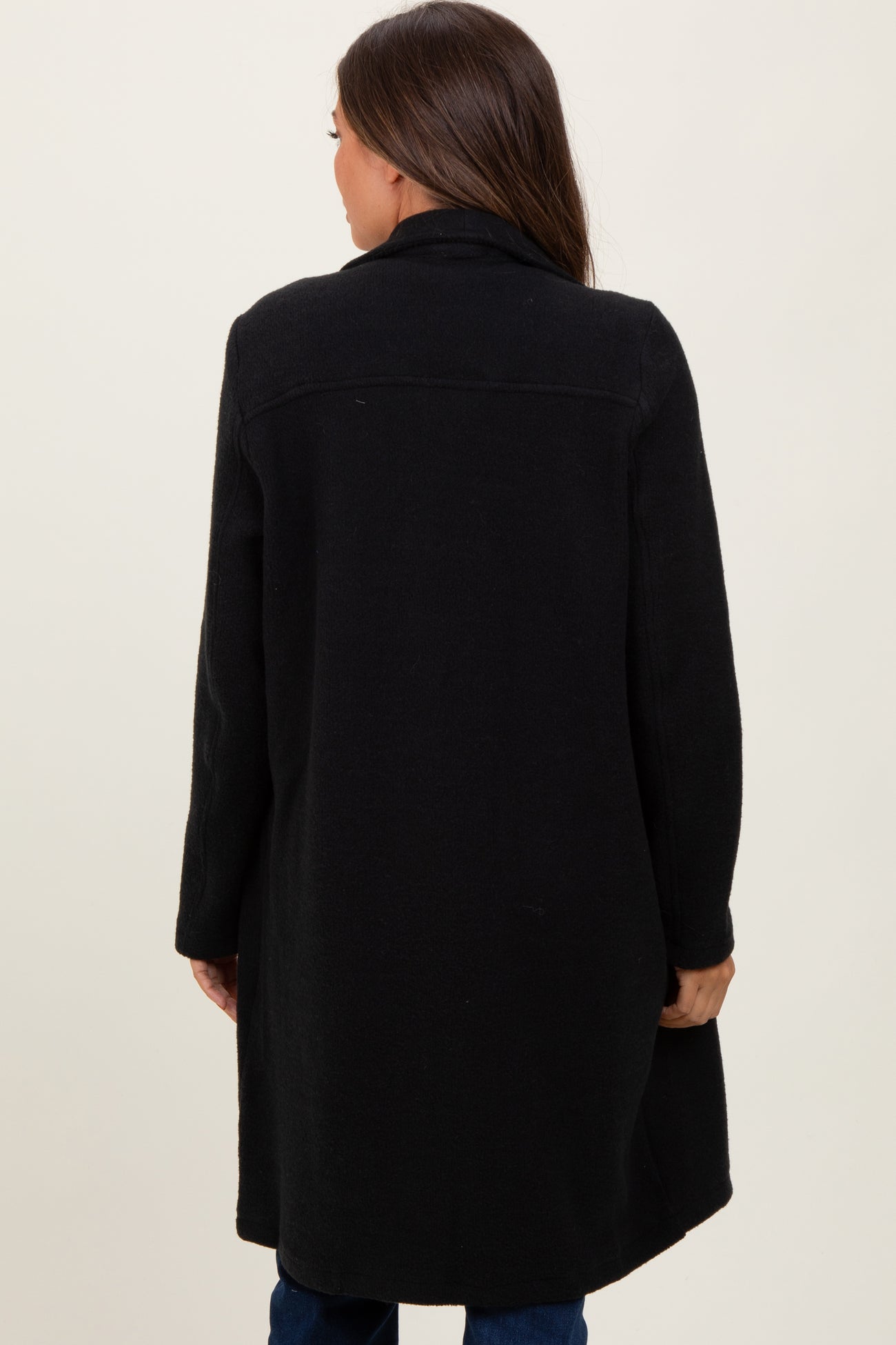 woman wearing a black maternity coat with a long, relaxed fit and a collar, viewed from the back