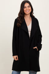 woman wearing a black oversized fleece coat with open front and side pockets, smiling against a neutral background