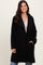woman wearing a black oversized fleece coat with open front and side pockets, smiling against a neutral background