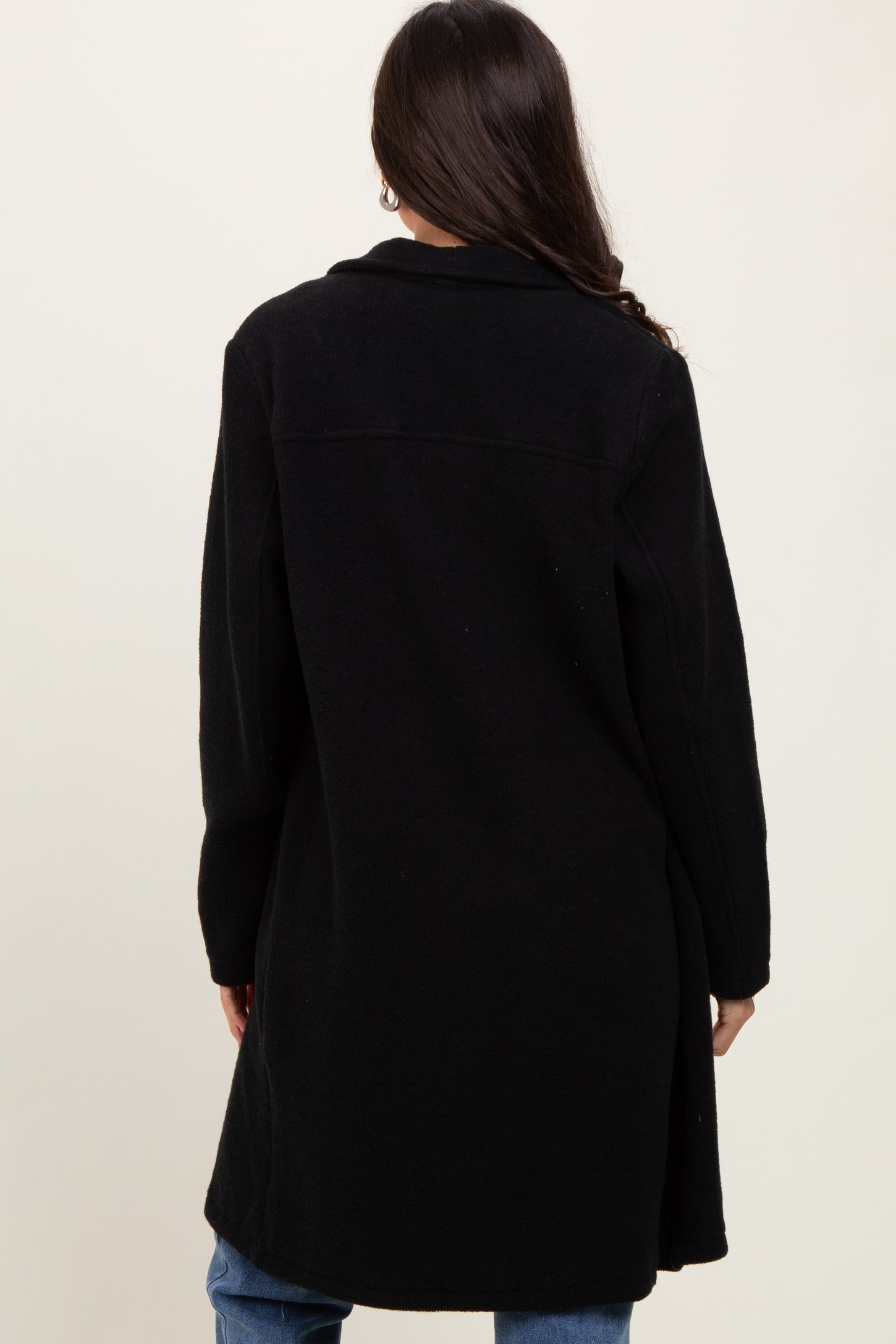 woman wearing a black long coat, viewed from the back, paired with blue jeans