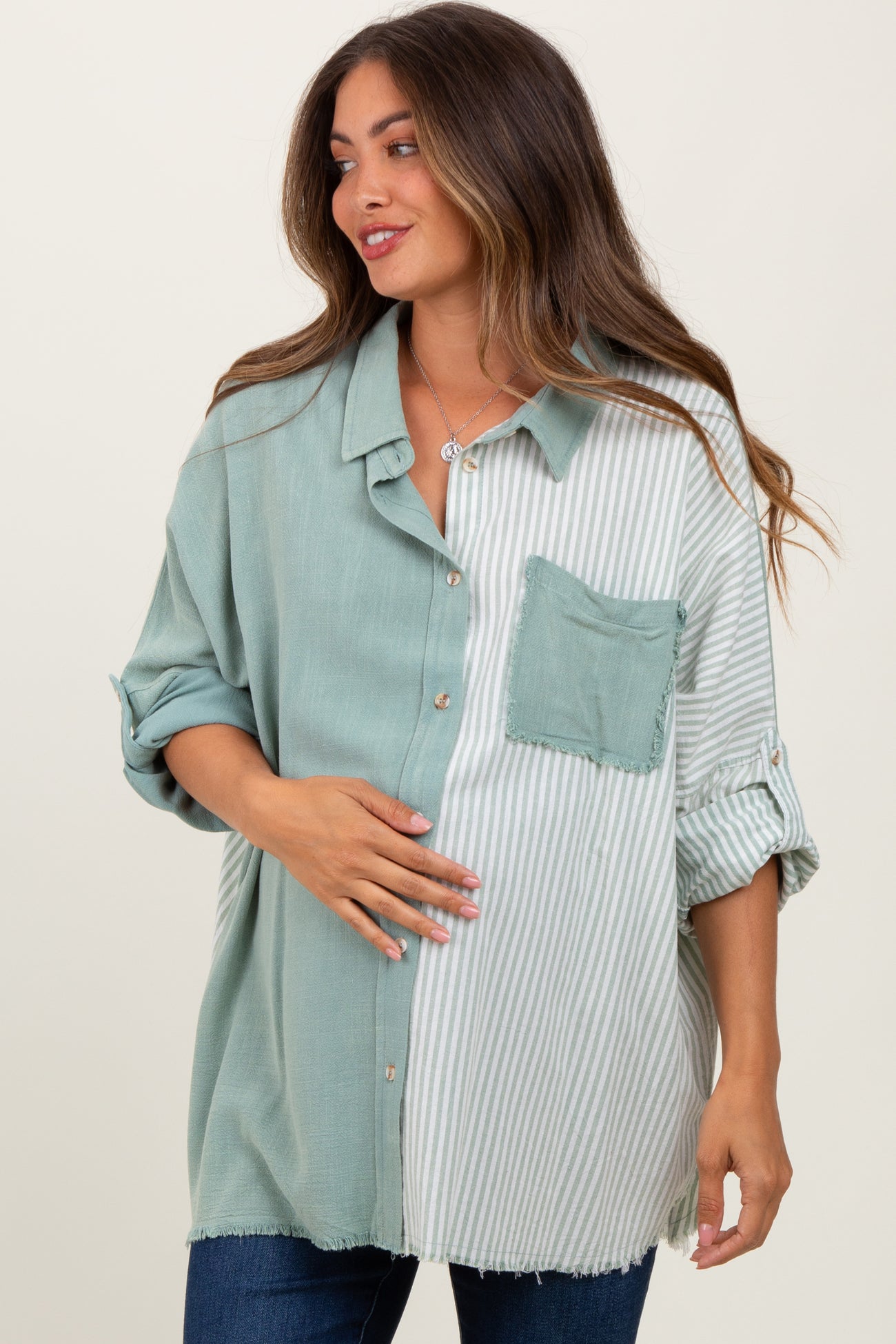 woman wearing a maternity green and white striped oversized button-up shirt and holding her baby bump