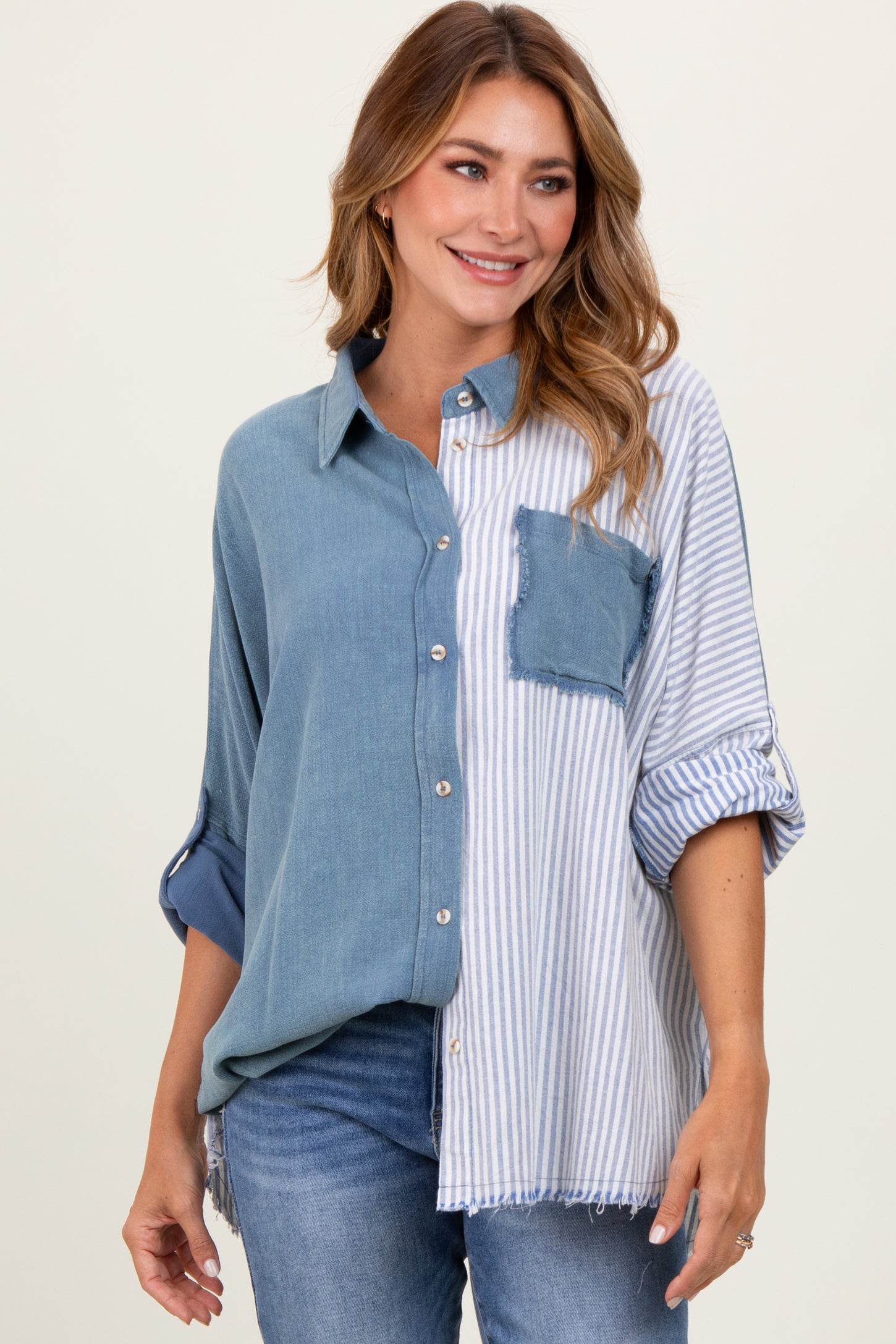 woman wearing a color-blocked oversized button-up shirt with denim and striped patterns, paired with blue jeans