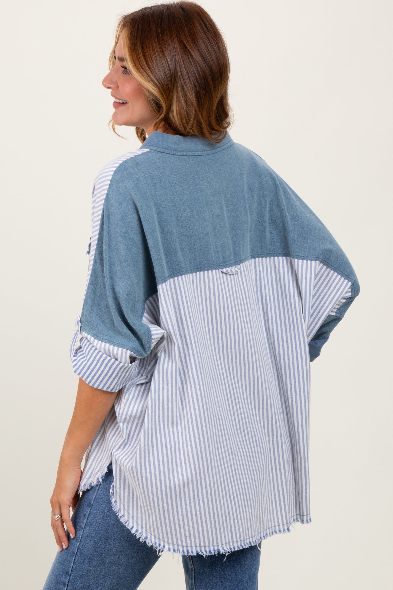 woman wearing a striped oversized shirt with a denim back and rolled sleeves, seen from the back