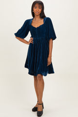 woman wearing a navy blue velvet short sleeve dress with a square neckline and button details, standing in black heels
