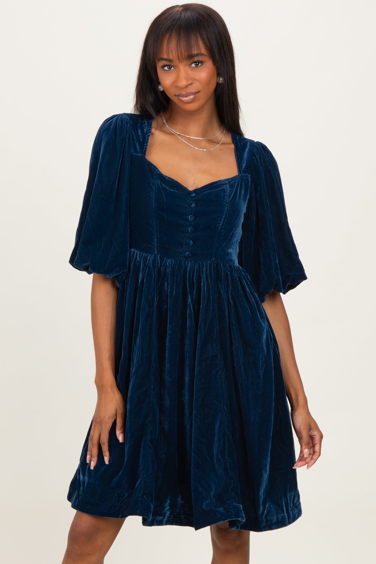 woman wearing a dark teal velvet short dress with puff sleeves and a fitted bodice, styled with a square neckline