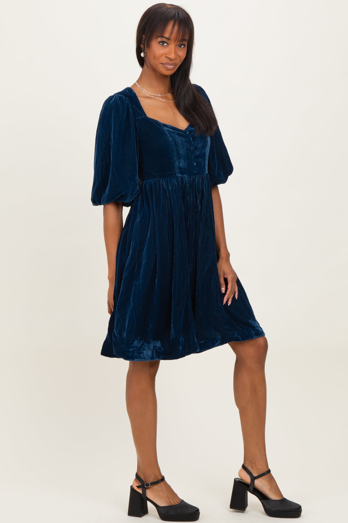 woman wearing a navy blue velvet short sleeve dress with a square neckline and puff sleeves