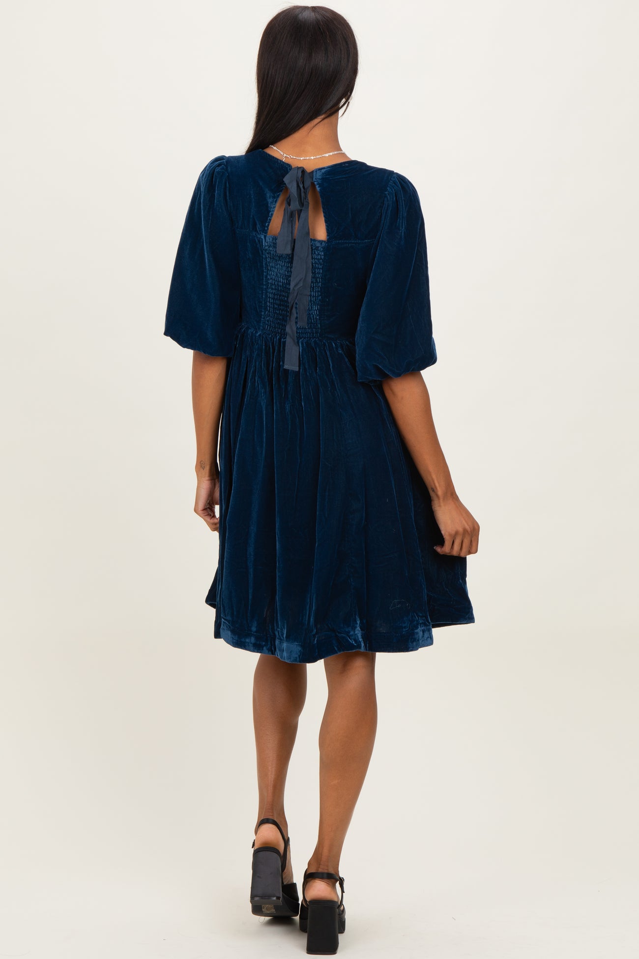 woman wearing a navy blue velvet dress with short puff sleeves and a bow detail at the back