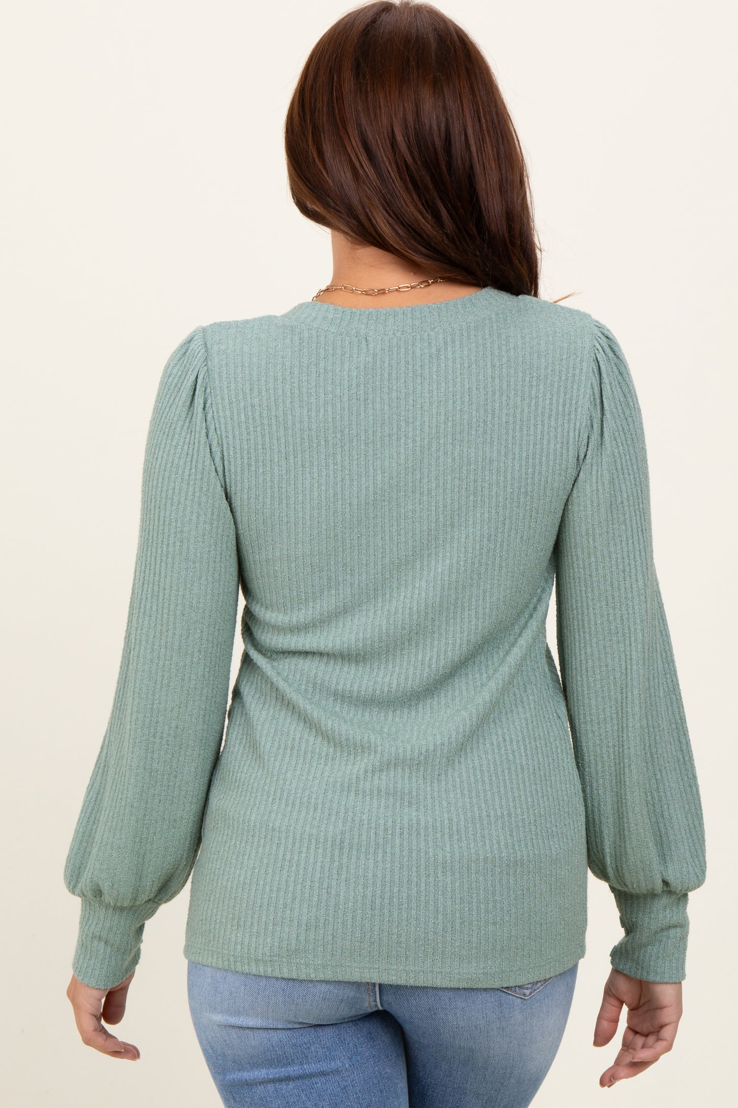 woman wearing a green ribbed long sleeve top with puff sleeves, seen from the back