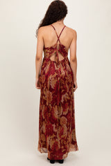 woman wearing a backless sleeveless maxi dress with a floral pattern in red and gold colors