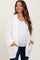 woman wearing a white knitted maternity cardigan over a white top, showing her baby bump while smiling