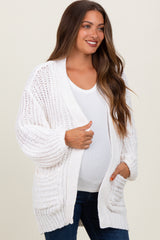 woman wearing a white open-knit maternity cardigan over a white top and showing her baby bump