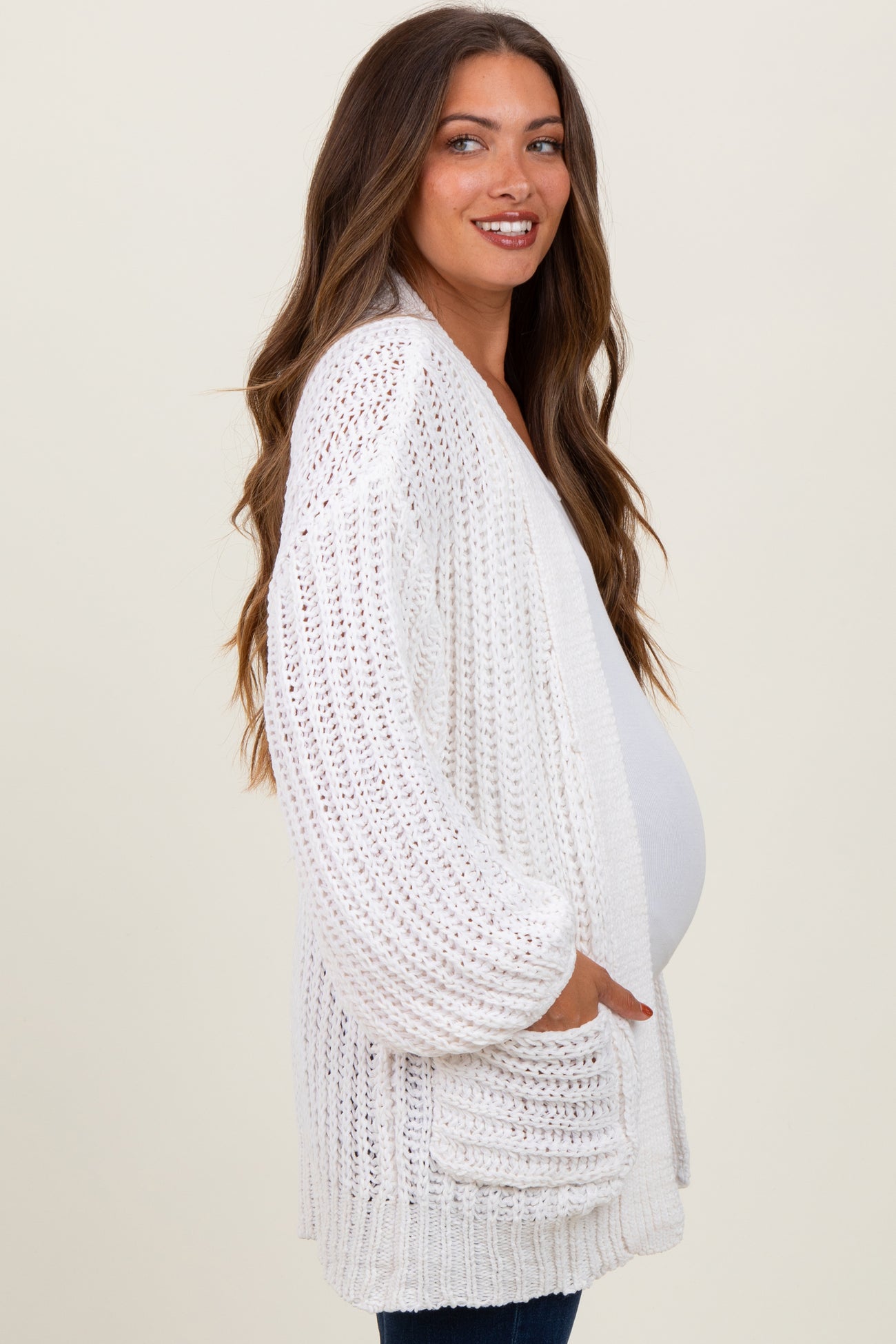 woman wearing a white open-knit maternity cardigan and showing her baby bump