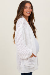 woman wearing a white open-knit maternity cardigan and showing her baby bump