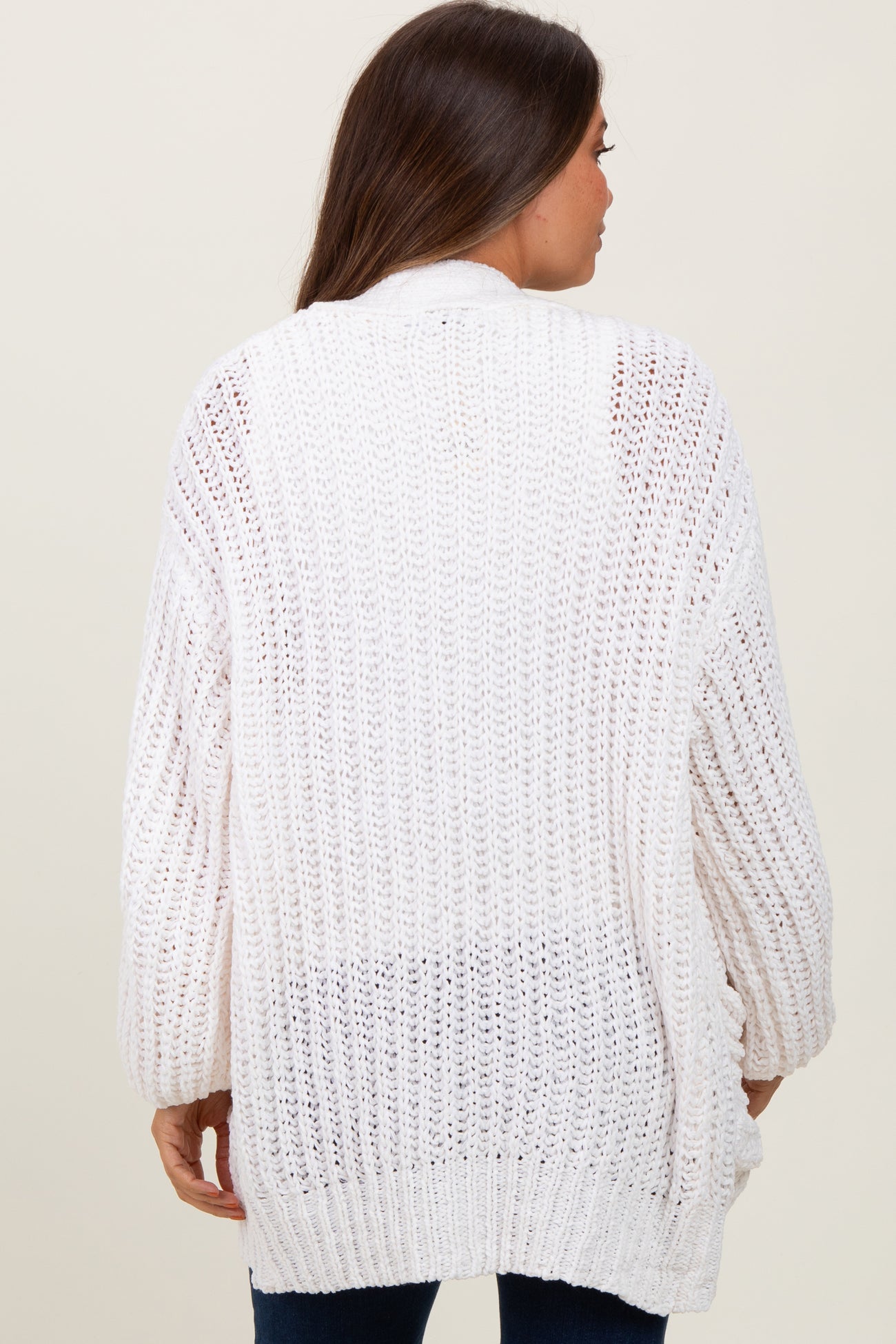 woman wearing a loose-fitting white knit maternity cardigan, showing the back view