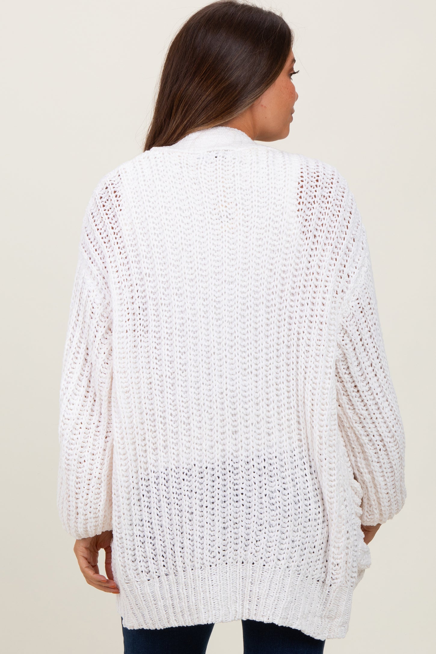 woman wearing a loose-fitting white knit maternity cardigan, showing the back view