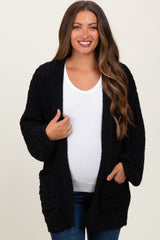 woman wearing a black chunky knit maternity cardigan over a white top and showing her baby bump