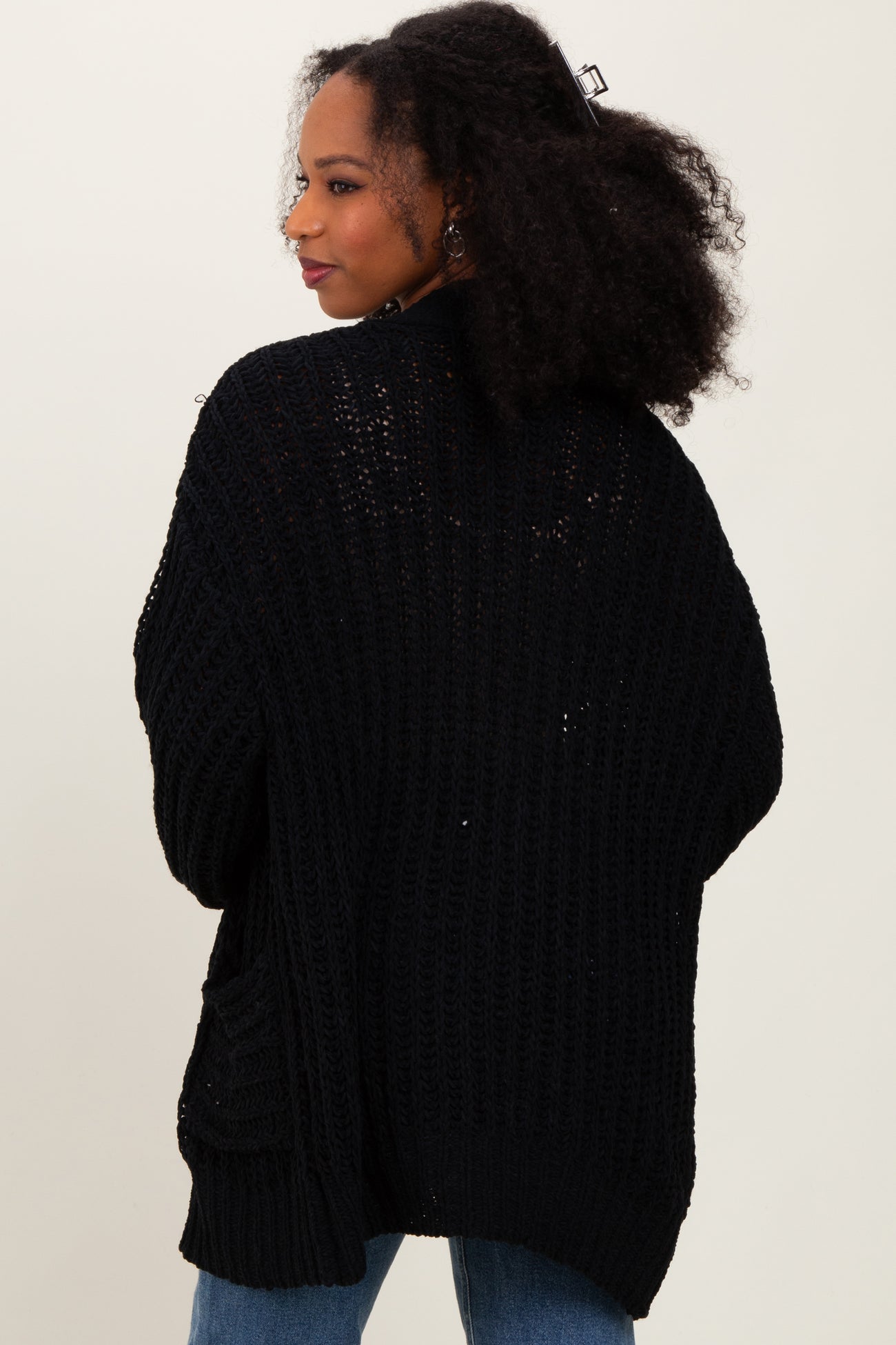 woman wearing a black oversized knit cardigan from the back, styled with a relaxed fit and side pockets