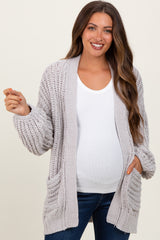 woman wearing a light grey chunky knit maternity cardigan over a white top, showing her baby bump
