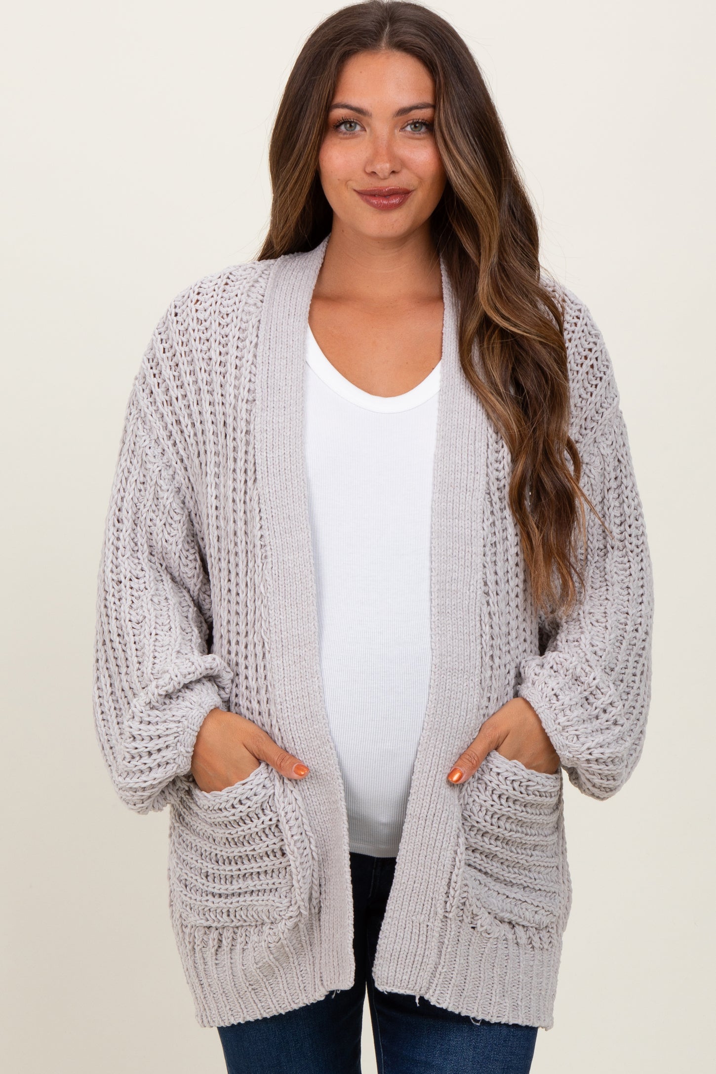 woman wearing a light gray knitted maternity cardigan with pockets and a visible baby bump