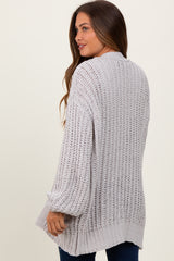 woman wearing a light gray open-knit maternity cardigan with long sleeves and a relaxed fit