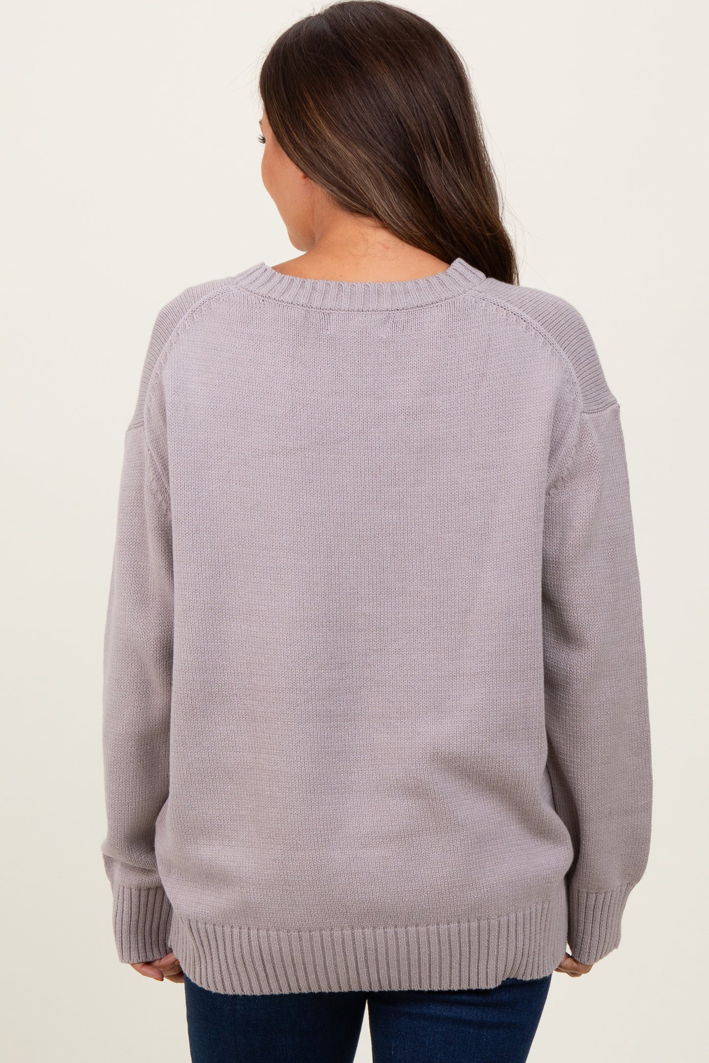 woman wearing a light gray oversized maternity sweater with a round neckline and ribbed cuffs, seen from the back