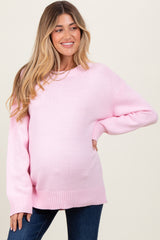 woman wearing a light pink oversized maternity sweater with a visible baby bump