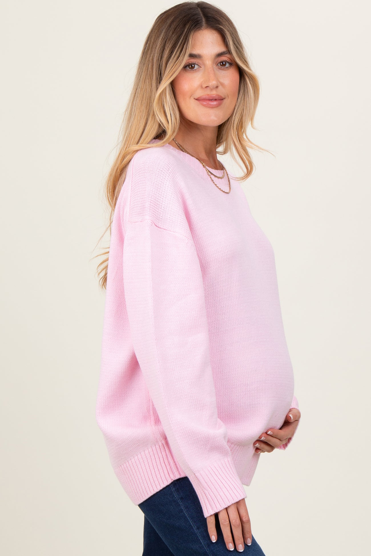 woman wearing a light pink oversized maternity sweater and holding her baby bump