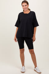 woman wearing a black oversized t-shirt with a pocket and black biker shorts, standing with hands on hips